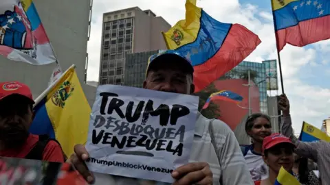 Getty Images A pro-government protester rallies against US sanctions with a sign reading "Trump unblock Venezuela" in Caracas on August 7, 2019