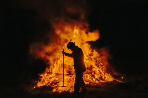 Cam Neville A firefighter, seen in silhouette, attends to a controlled fire with a rake