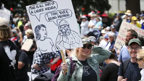 Getty Images Anti-lockdown protester in New Zealand holds up a banner saying it's all part of a larger agenda