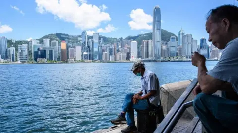 Getty Images A man sits along the Kowloon side of Victoria Harbour which faces the skyline of Hong Kong Island.