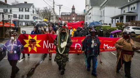 Getty Images Demonstrators march through Plymouth on Thanksgiving in 2020, holding a large red banner that says 'National Day of Mourning.'