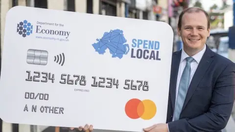 Department for the Economy Gordon Lyons holding a giant Spend Local card