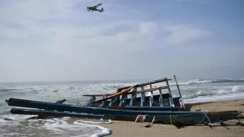 EPA Broken pieces of a boat on a beach, as a plane flies overhead