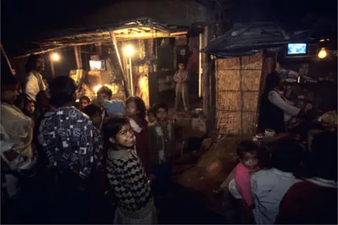 Getty Images People in the streets gather around shops with televisions at night in January of 1999 in the slums of New Delhi, India.