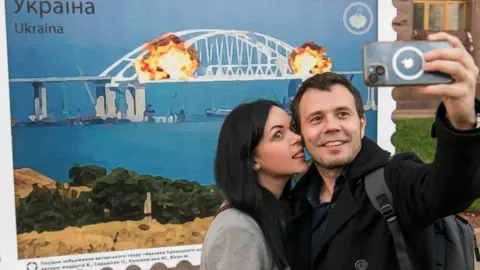 EPA A woman and man pose in front of an artist's impression of the Crimean bridge explosion in Kyiv, Ukraine