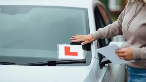 Getty Images Woman sticking an L plate on her car