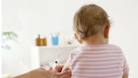 Getty Images A baby girl shown just before receiving a vaccine (file photo)