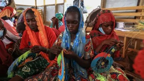 Getty Images A group of women make fans in a workshop given by members of the NGO, Plan International, during a visit by Filippo Grandi, the United Nations High Commissioner for Refugees (UNHCR), in Maroua on April 28, 2022