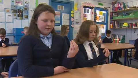 Two 10 year old girls holding a closed hand in the air with their eyes closed