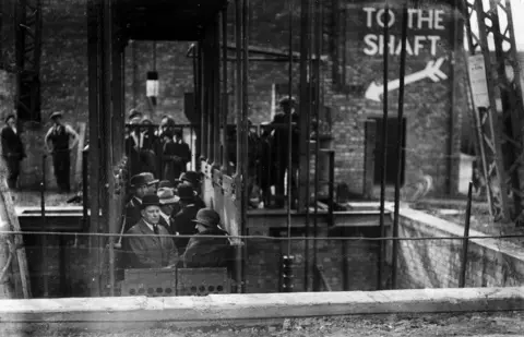 Getty Images Black and white image of people standing in cage descending into the mine shift display