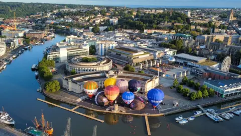 PA Media Hot air balloons inflate and tether from Bristol Harbourside as the countdown begins to the 2023 Bristol International Balloon Fiesta at Ashton Court Estate in August.