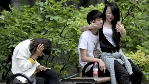 Getty Images A couple use a mobile phone to take a picture at a park in Beijing