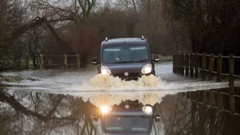 PA Media A car makes its way along a flooded road in Mountsorrel, Leicestershire