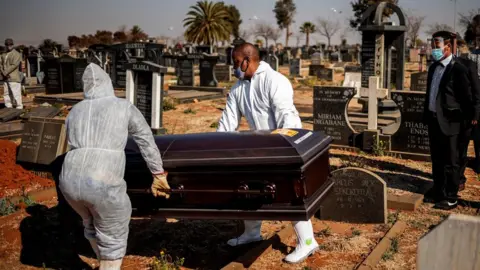 AFP Relatives observe undertakers moving a casket containing the remains of a COVID-19 coronavirus patient during a funeral at the Avalon cemetery in Soweto, on July 24, 2020.