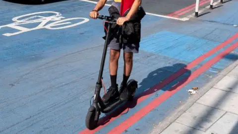 Getty Images Man shown from neck down riding an e-scooter in a cycle lane on a London road.