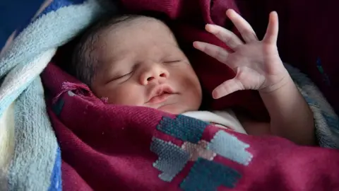 Indian mother Sonia looks on as her newborn baby girl stretches at a government hospital in Amritsar on July 11, 2013, on the occasion of World Population Day. 