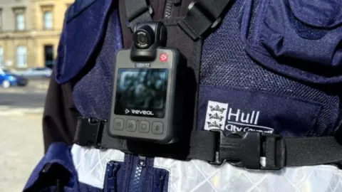 A body camera, about the size of a mobile phone, on the front of a Hull parking officer's navy blue jacket. 