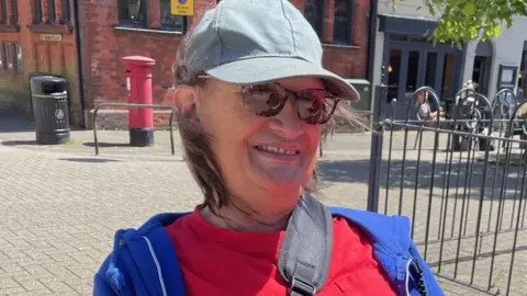 Martine is white and wearing a blue cap, sunglasses, a red T-shirt and a blue hoodie