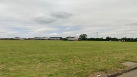 View of the site which is an open field with football goals and housing in the distance