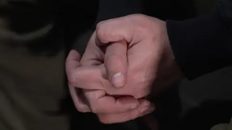 Close up of Adam's hands clasped together. Very little else can be seen, other than his black sleeves.