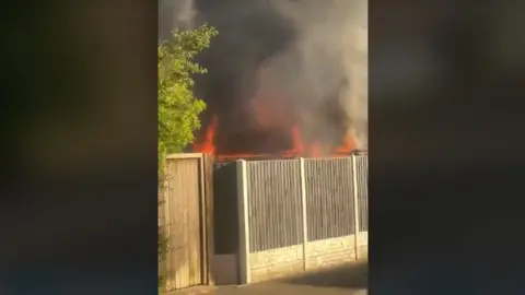 Tanisha Gijare Smoke and orange flames can be seen above and behind a wooden fence