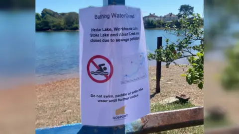 A piece of A4 laminated paper which says: Bathing water closed. Haslar Lake, Workhouse Lake, Stoke Lake and Alver Creek are closed due to sewage pollution. Do not swim, paddle or enter the water until further notice. Gosport Borough Council."