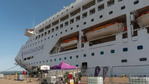 Getty Images A large cruise ship, photographed from the dock-side at Invergordon. It has the words Ambassador Cruise Line on the side, next to three lifeboats.