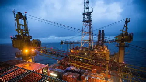 Offshore oil platform lit up by lights standing alone in the sea under a cloudy sky