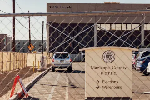 Getty Images Fence and gate in front of the parking lot with a sign on it "Maricopa County" and has arrows to the election camp