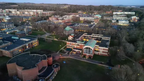 Getty Images Aerial view of the University of Sussex campus at dusk, in winter, with modern red-brick buildings, pathways and surrounding woodland.