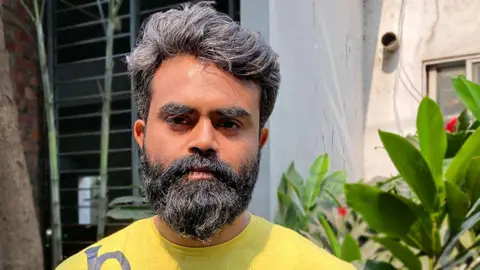 Momina Raman Royal wearing a yellowish  t-shirt and sporting a afloat  beard