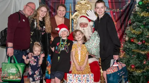 Family photo Lilly and Rachel with the Hamer family posing with Santa and gifts at the event. Lilly's other three brothers and father are also pictured. 