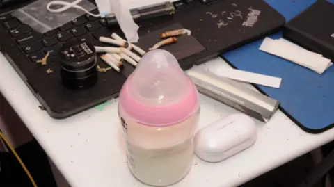 Kent Police A baby's bottle filled with milk sits on a desk, next to a computer keyboard, covered in cannabis joints and cigarette papers.