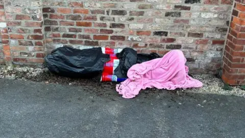 York BID Great Britain Nutcracker wrapped up in plastic bags and a pink blanket by a brick wall.