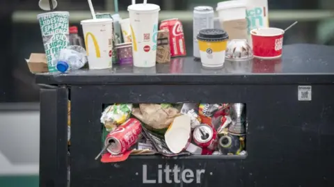 A close-up of a full litter bin, with cartons and cups perched on the top
