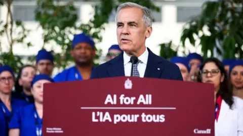 Canada's Prime Minister Mark Carney announces a new federal AI agenda, at Toronto General Hospital. He is standing in front of several healthcare workers who are wearing scrubs and lab coats. He stands behind a podium that says "AI for All - L'IA pour tous". 