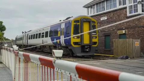 Northern Train at station with level crossing barrier in the foreground