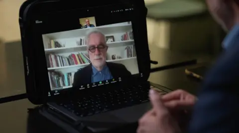 Moreno Ocampo is shown on a laptop screen talking in a video chat with a BBC reporter