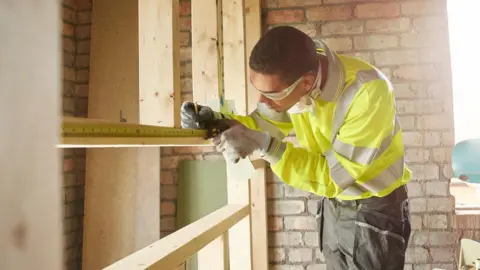 Getty Images A young male carpenter measuring wooden stud work on a housing site