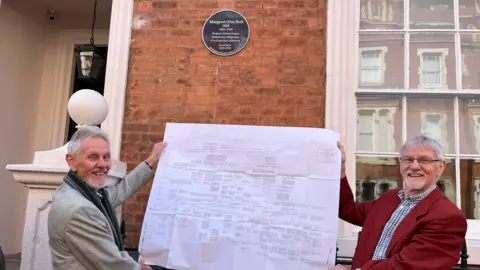 Bruce and Malcolm Glen Bott stood in front of plaque holidng large family tree document