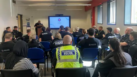 Photograph of Greater Manchester Police officers attending a briefing for Operation Avro. The image shows the backs of police officers, taken from behind.