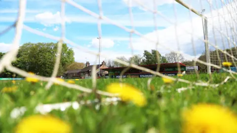 Getty Images A football pitch viewed through the net within one of the goals. Yellow flowers can be seen close up amongst the grass.