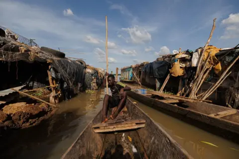 OUSMANE MAKAVELI/AFP A boy uses a pirogue to move between houses submerged in water in the flooded area of the Badalabougou district in Bamako on 3 October, 2024. 