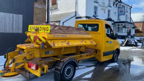 Shropshire Council A yellow van with a spreader on the back, outside a pub in the snow