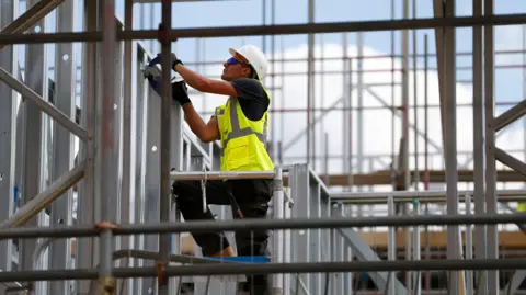 Reuters A male construction worker on a building site wearing a hard hat and a yellow high visibility jacket
