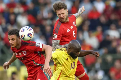 PA Media Wales footballers Joe Rodon and Ethan Ampadu are either side of Belgium's Romelu Lukaka as they challenge for the ball. Rodon has leapt in the air to head the ball and has his eyes closed while leaning on the back of Lukaku