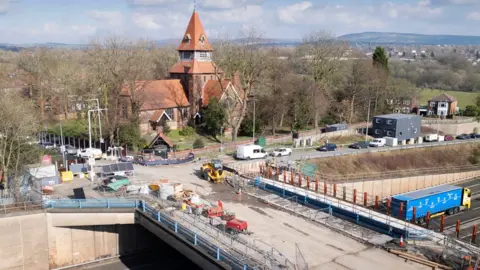 HE Church of St Anne, St Anne's Drive, Haughton, Denton, Greater Manchester. Exterior, view from north showing National Highways work to bridge on M67 to the south of the church