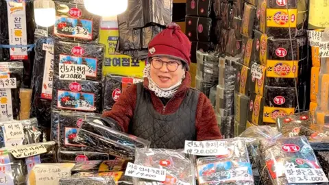 BBC/Suhnwook Lee A woman standing in front of a seaweed shop 