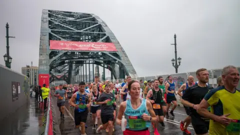 Getty Images Hundreds of runners, wearing different coloured vests, cross the Tyne Bridge in the rain during the 2024 Great North Run.