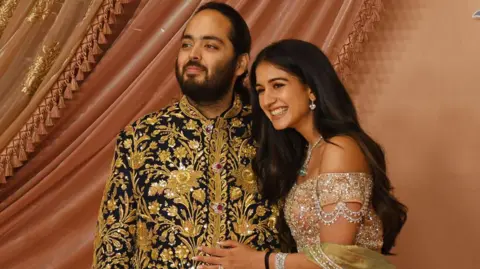 Getty Images MUMBAI, MAHARASHTRA, INDIA - 2024/07/05: Anant Ambani (son of Indian businessman Mukesh Ambani) and his fiancée Radhika Merchant pose for a photo on the red carpet during the sangeet ceremony at Jio World Centre in Mumbai. (Photo by Ashish Vaishnav/SOPA Images/LightRocket via Getty Images)